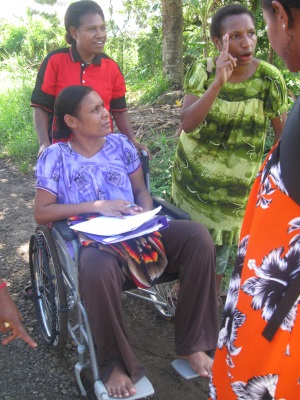 Picture of three women from Papua New Guinea collecting information about road use. One of the women is using a wheelchair and has data sheets on her lap.