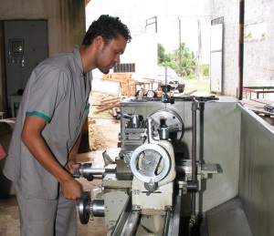 Picture of a young man from Brazil who is deaf, in a workshop using a lathe. 