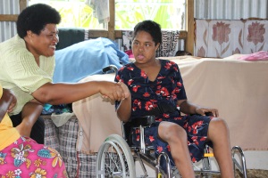 Picture of a girl from Fiji seated in a wheelchair, shaking hands with a woman representative from the Fiji Disabled Persons Federation.