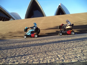 Picture of two women from using motorised scooters driving past the Sydney opera house.